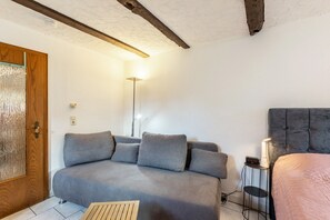 A room with a grey sofa, a bedside table with a lamp, a bed with a headboard, and a wooden door. - Apartment Schlossmühle in Bigge-Olsberg (Olsberg)