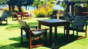 An outdoor seating area with tables and chairs, surrounded by tropical plants and palm trees. - Côté Sud Pousada de Charme (São Miguel dos Milagres)