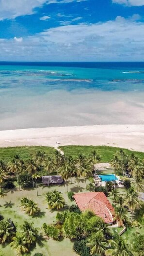 An aerial view of a beach resort with a clear view of the ocean, a sandy beach, and a cluster of palm trees. - Côté Sud Pousada de Charme (São Miguel dos Milagres)