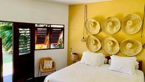 A bedroom with a bed, a chair, and a wall decorated with hats. - Côté Sud Pousada de Charme (São Miguel dos Milagres)