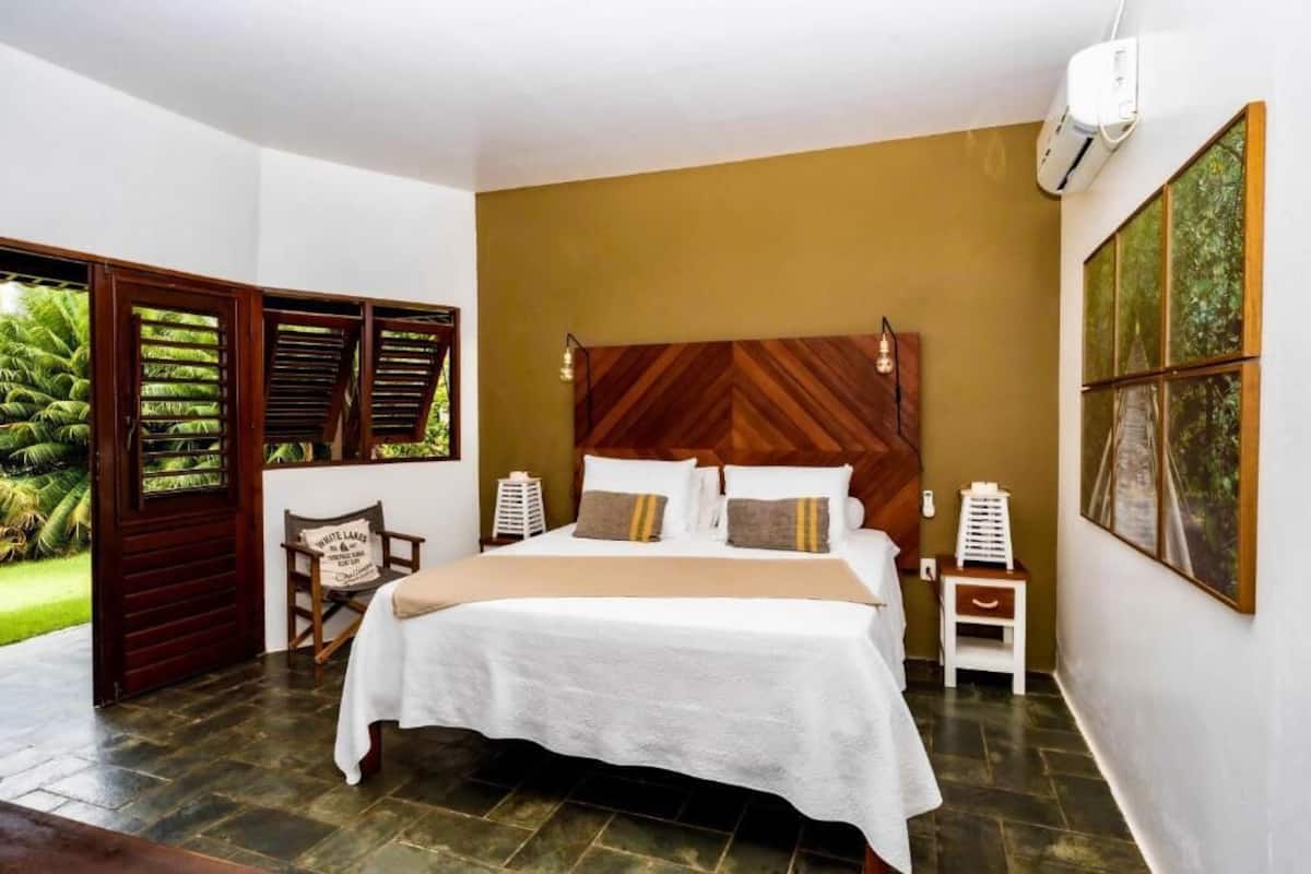 A bedroom with a large bed, a wooden headboard, a nightstand, a chair, and a painting on the wall.