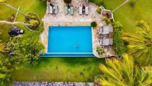 An aerial view of a swimming pool with lounge chairs and a stone deck, surrounded by greenery and palm trees. - Côté Sud Pousada de Charme (São Miguel dos Milagres)