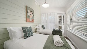 A bedroom with two beds, a painting, a window with blinds, and a ceiling light. - Inchcolm – Your Quintessential Blue Mountains Getaway (Leura)