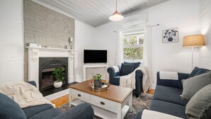 A living room with a fireplace, a television, and two sofas. - Inchcolm – Your Quintessential Blue Mountains Getaway (Leura)