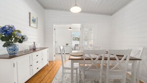 A bright, white interior with a wooden dining table and chairs, a vase with flowers, and a hanging light fixture. - Inchcolm – Your Quintessential Blue Mountains Getaway (Leura)
