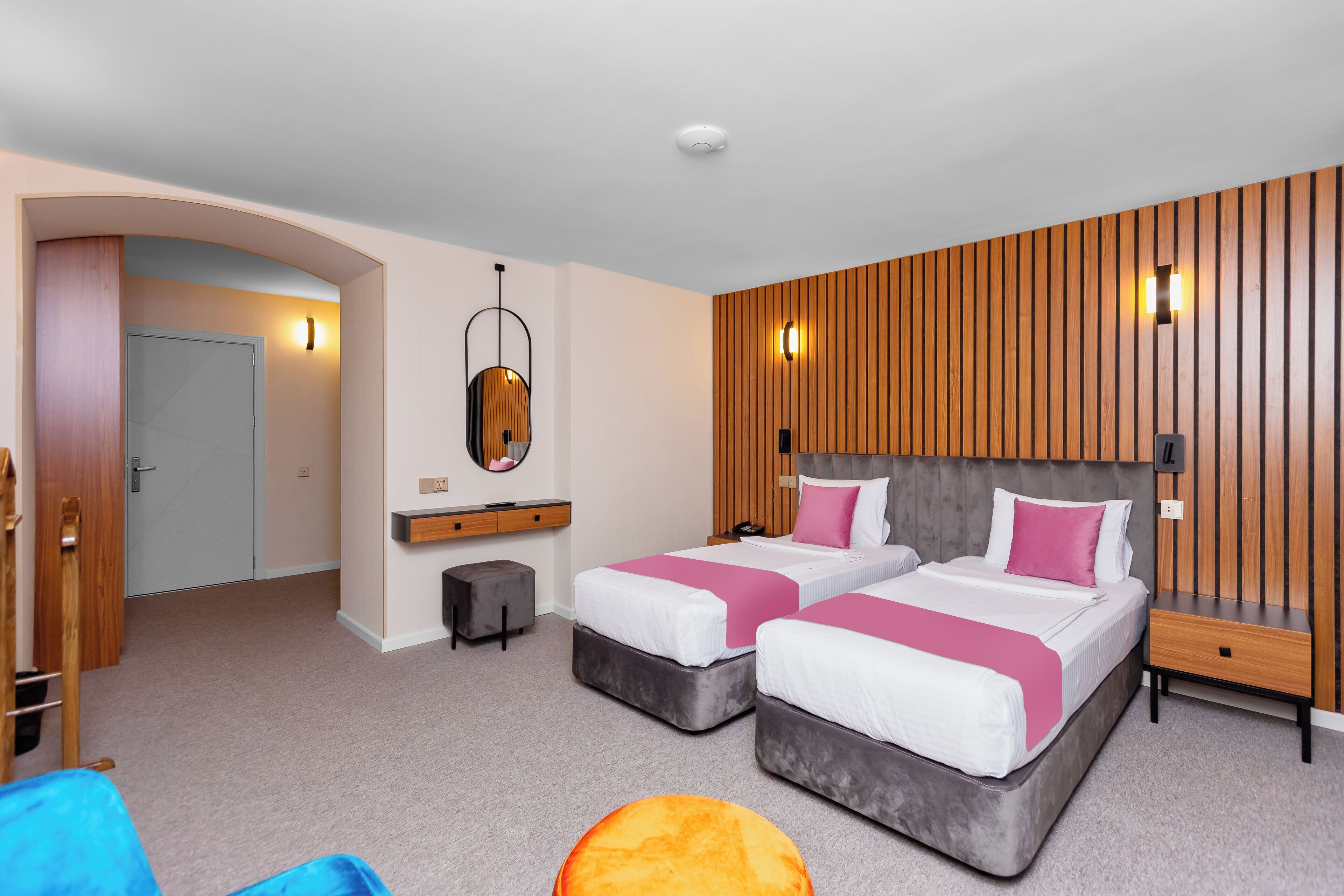 A modern bedroom with two beds, a wooden accent wall, and a small seating area.