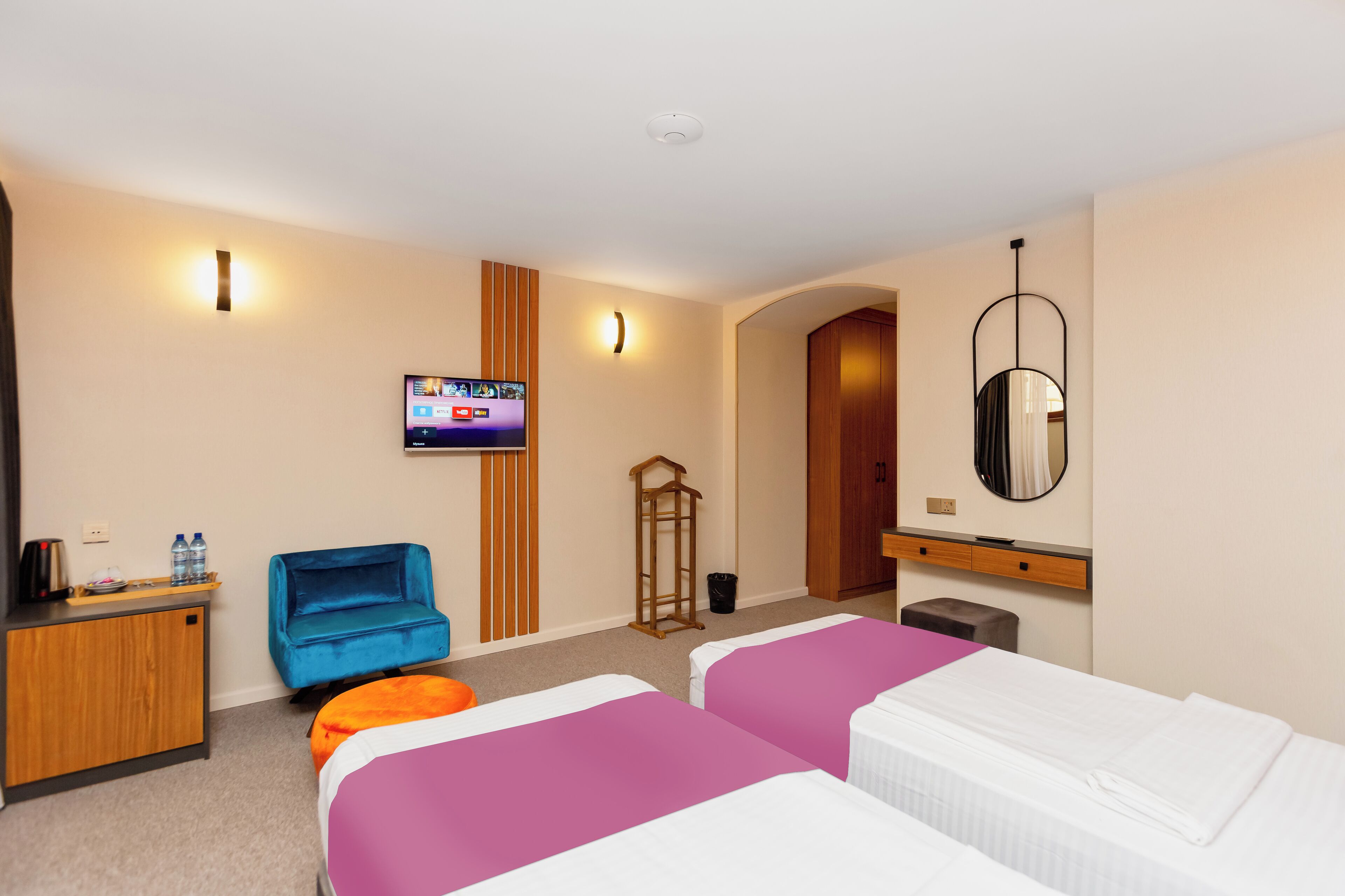 Una camera d'albergo con due letti, una scrivania, una televisione, uno specchio e un piccolo angolo salotto.