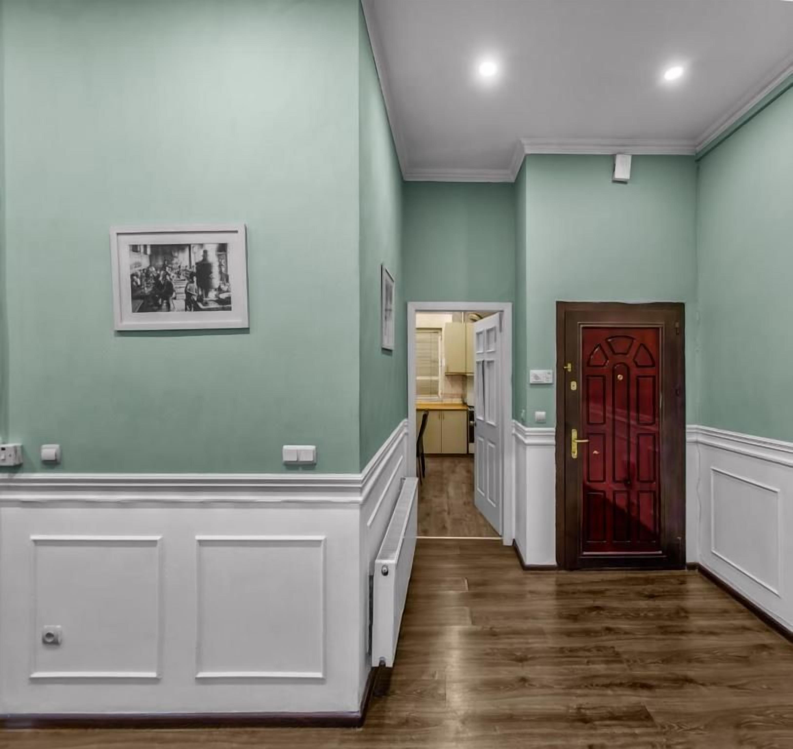 A hallway with a wooden floor, a red door, and a framed picture on the wall.
