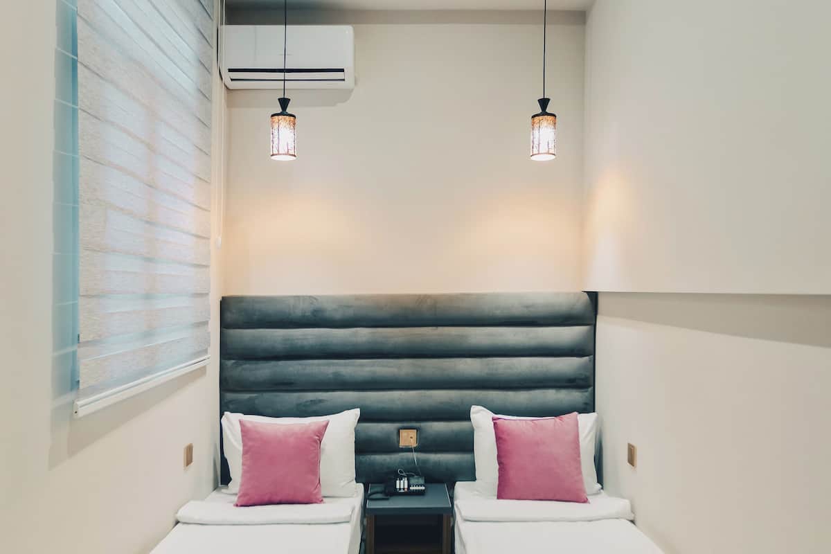 A small, modern room with two single beds, a dark headboard, and a window with blinds.