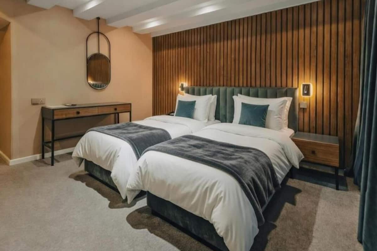 A double bed with two pillows, a bedside table, a mirror, and a wooden panel wall.