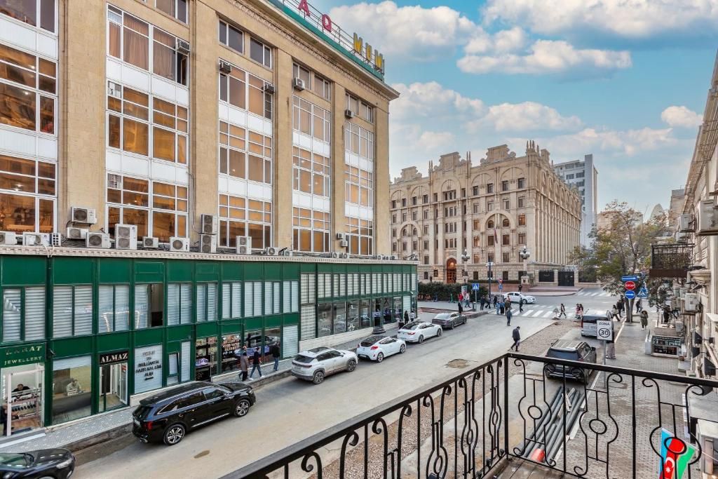 Straßenansicht mit einem Gebäude mit mehreren Geschäften, darunter ein Juweliergeschäft, und einem großen, verzierten Gebäude im Hintergrund.