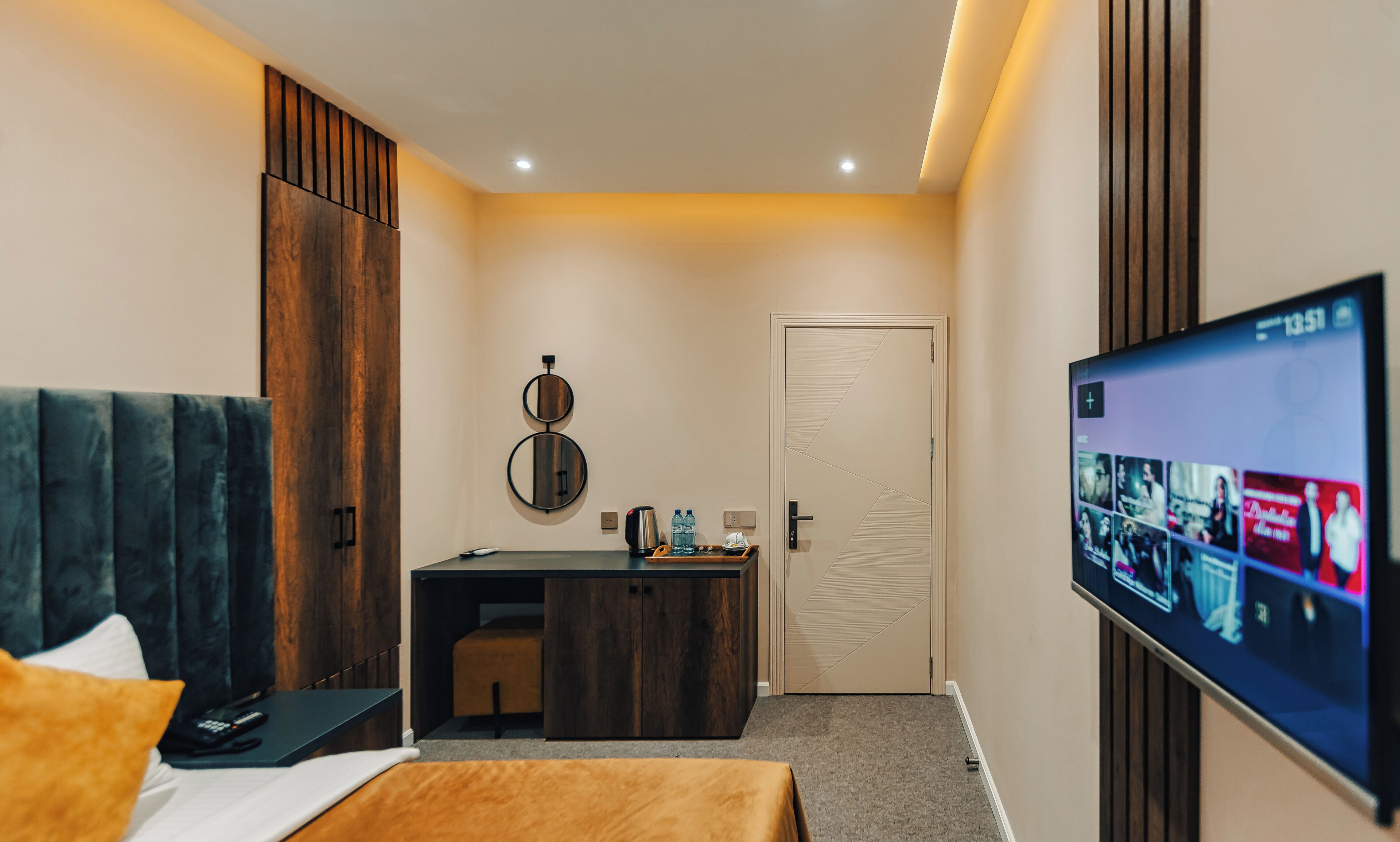 A hotel room with a bed, desk, TV, and a door.
