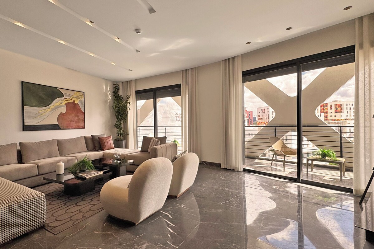 Una sala de estar moderna con sofá, sillones, una mesa de centro y un amplio ventanal con vistas a edificios.