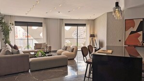 A modern living room with a sofa, armchairs, a coffee table, and a dining area with a bar. Large windows provide a view of the cityscape. - Hotel Soho Boutique Casablanca (Casablanca)
