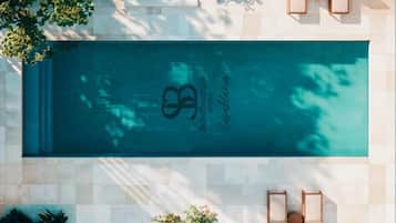 Piscina no terraço com logotipo, rodeada por espreguiçadeiras e plantas em vasos.