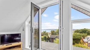 A room with a large window, a television on a wooden stand, and a view of a residential area. - Swanston Lodge in Paignton (Paignton)