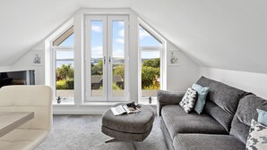 A modern loft bedroom with a large skylight, a grey sofa, a white armchair, and a small table with a book and glasses. - Swanston Lodge in Paignton (Paignton)