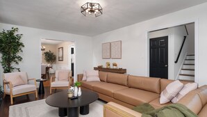 En stue med en beige sofa, to lænestole, et sofabord og en stor plante.