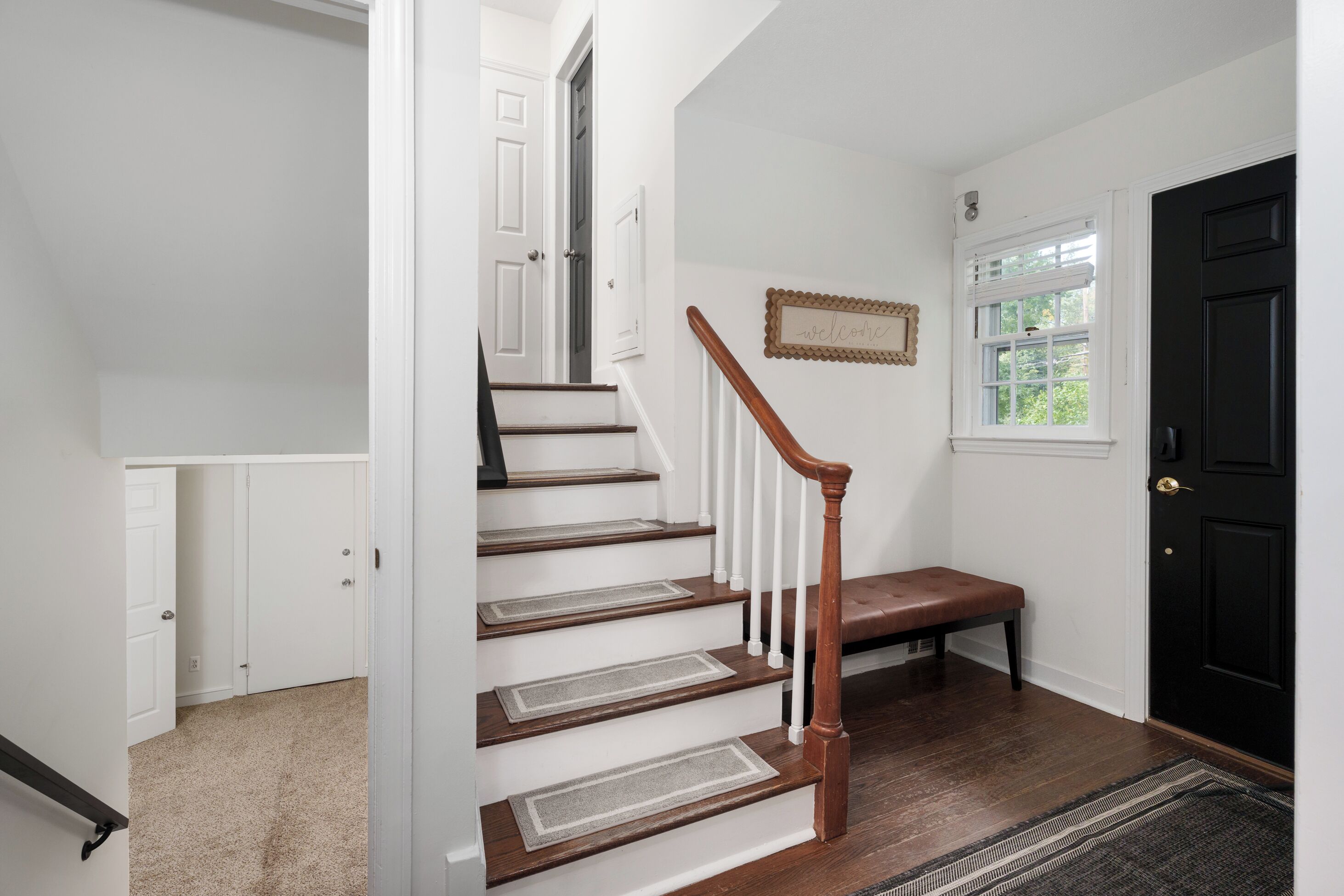 A staircase with wooden steps and a white handrail, leading to a landing with a bench and a door.