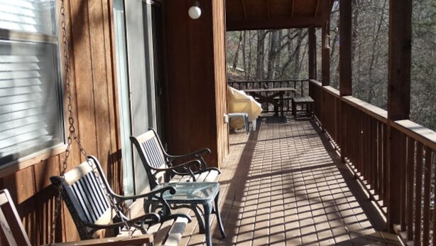 A wooden deck with a tiled floor, two chairs, a small table, and a view of trees.