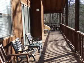 Une terrasse en bois avec un sol carrelé, deux chaises, une petite table et une vue sur les arbres.