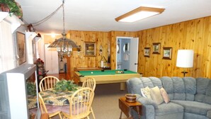A cozy living room with a pool table, a sofa, and a television.