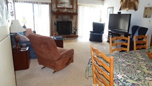 A living room with a fireplace, a television, a dining table with chairs, and a large fur rug on the floor.