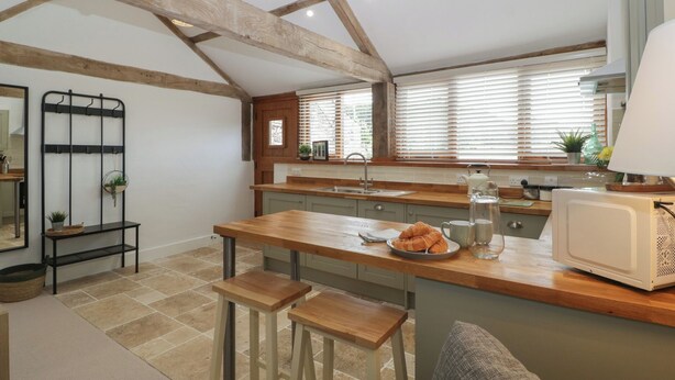 Una cocina con encimera de madera, un fregadero y un microondas blanco. Hay taburetes y una planta colgante.