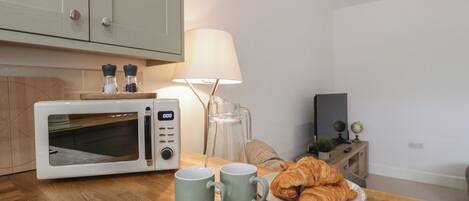 A kitchen with a microwave, two mugs, a plate of croissants, and a lamp.