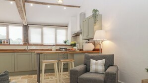 Una cocina acogedora con encimera de madera, dos taburetes, un sillón gris y una lámpara.