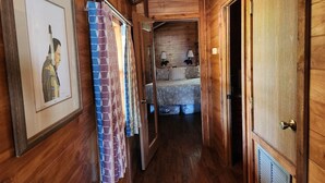 Een houten gang die leidt naar een slaapkamer met een bed, twee bedlampen en een ingelijste foto aan de muur.