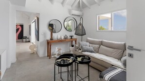 Ein modernes Wohnzimmer mit hoher Decke, einem Holzkonsolentisch, einem beigefarbenen Sofa und einem großen Fenster.