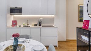 Cocina moderna con armarios blancos, microondas integrado y comedor con mesa redonda para dos.