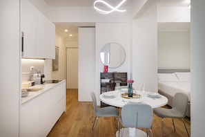 Una cocina moderna con armarios blancos, una mesa de comedor para cuatro personas y un espejo redondo sobre la mesa.