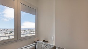Habitación con un ventanal grande que ofrece vistas a la ciudad, un pequeño sofá y una lámpara en una mesita de noche.