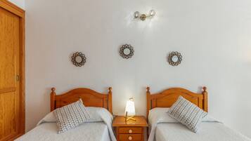 A bedroom with two beds, a nightstand with a lamp, and wall-mounted decor.