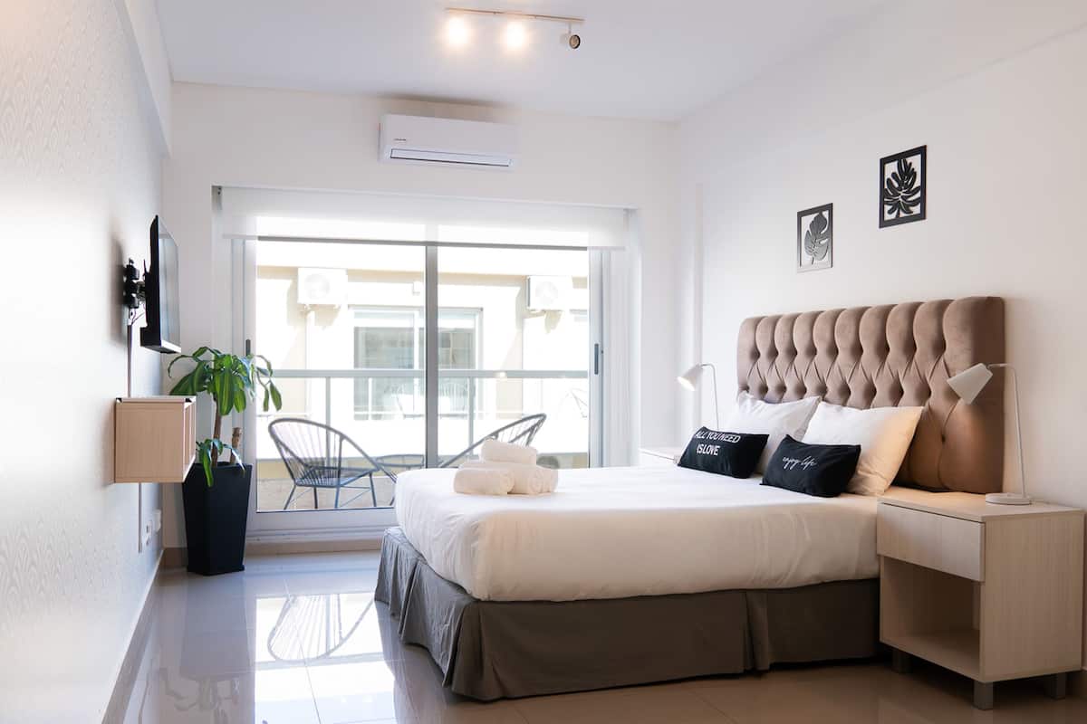 Een moderne hotelkamer met een groot bed, nachtkastje, stoel, een potplant en uitzicht naar buiten.