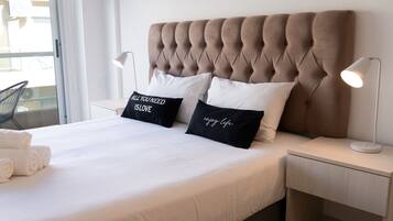 A neatly made bed with white bedding and two black pillows, one with text, in a modern room with a tufted headboard and bedside lamps.