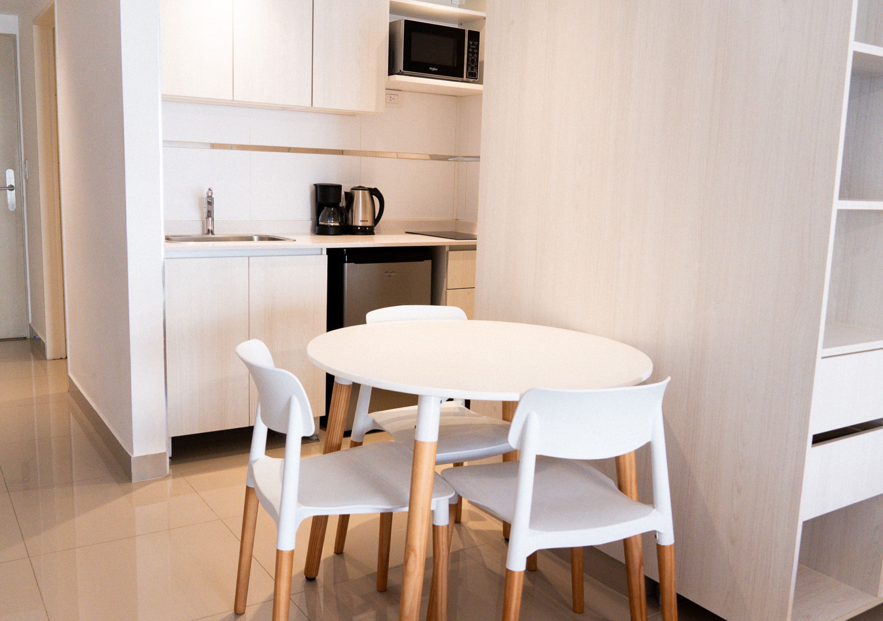 Uma cozinha compacta com uma mesa e cadeiras brancas, micro-ondas e cafeteira.