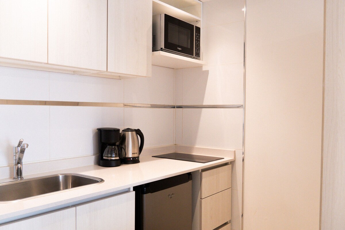 Cocina moderna con un lavamanos de acero inoxidable, una cafetera y un microondas sobre una encimera blanca.