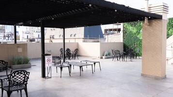 Zona exterior amb terrassa, taules i caires, zona de seients coberta i senyal de prohibició de fumar.