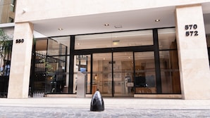 Un edificio moderno con entrada de vidrio, números 570 y 572, y un bolardo negro en la parte frontal.