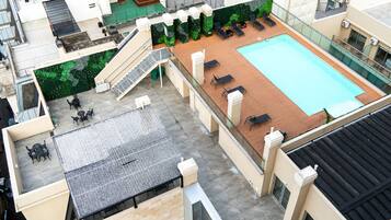 A rooftop pool area with lounge chairs, a small staircase, and a green wall.