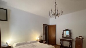 Een slaapkamer met een bed, nachtlampjes, een houten deur, een spiegel en een kroonluchter.
