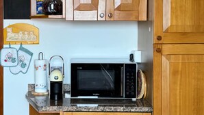 Een keuken met houten kastjes, een magnetron, een koffiezetapparaat en een rekje voor kruiden.
