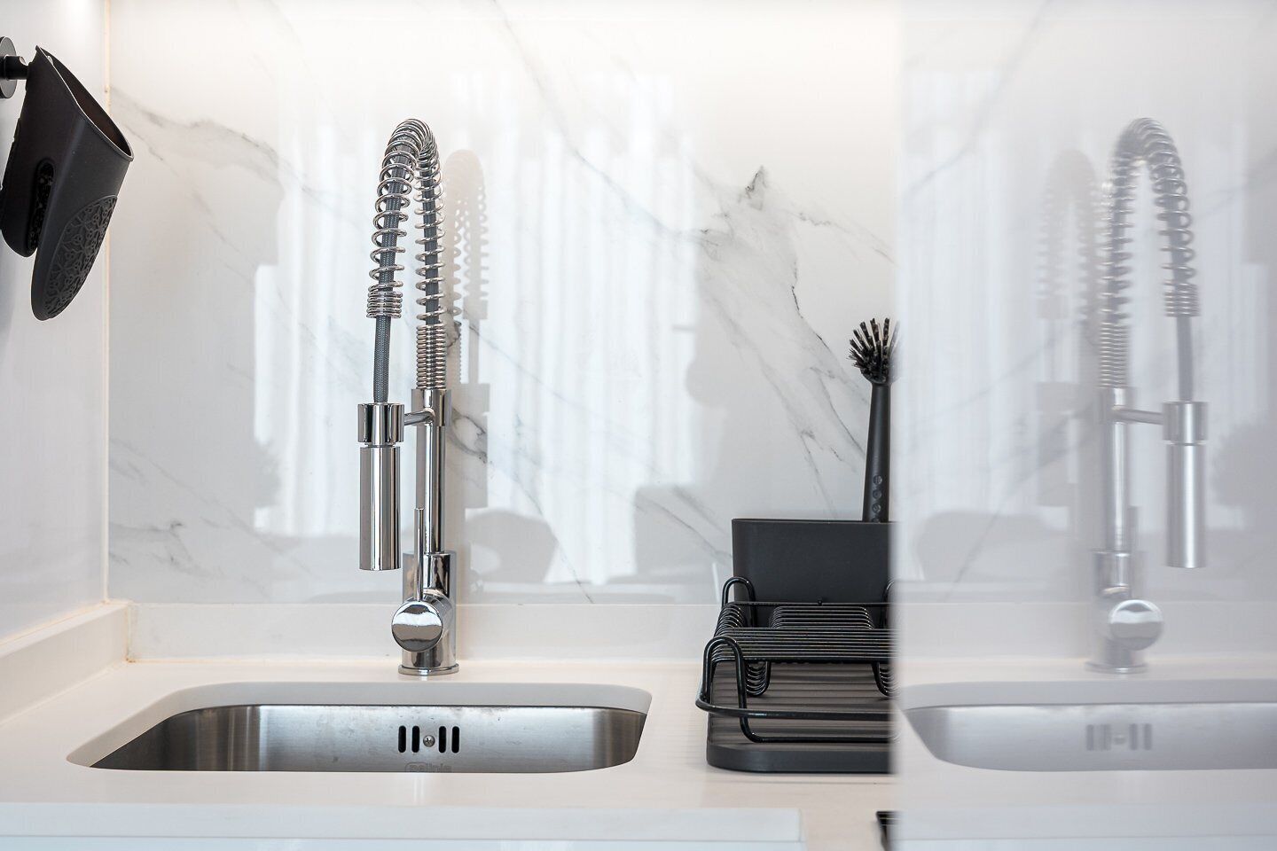 A modern kitchen with a stainless steel sink, a faucet with a flexible hose, and a black utensil holder.