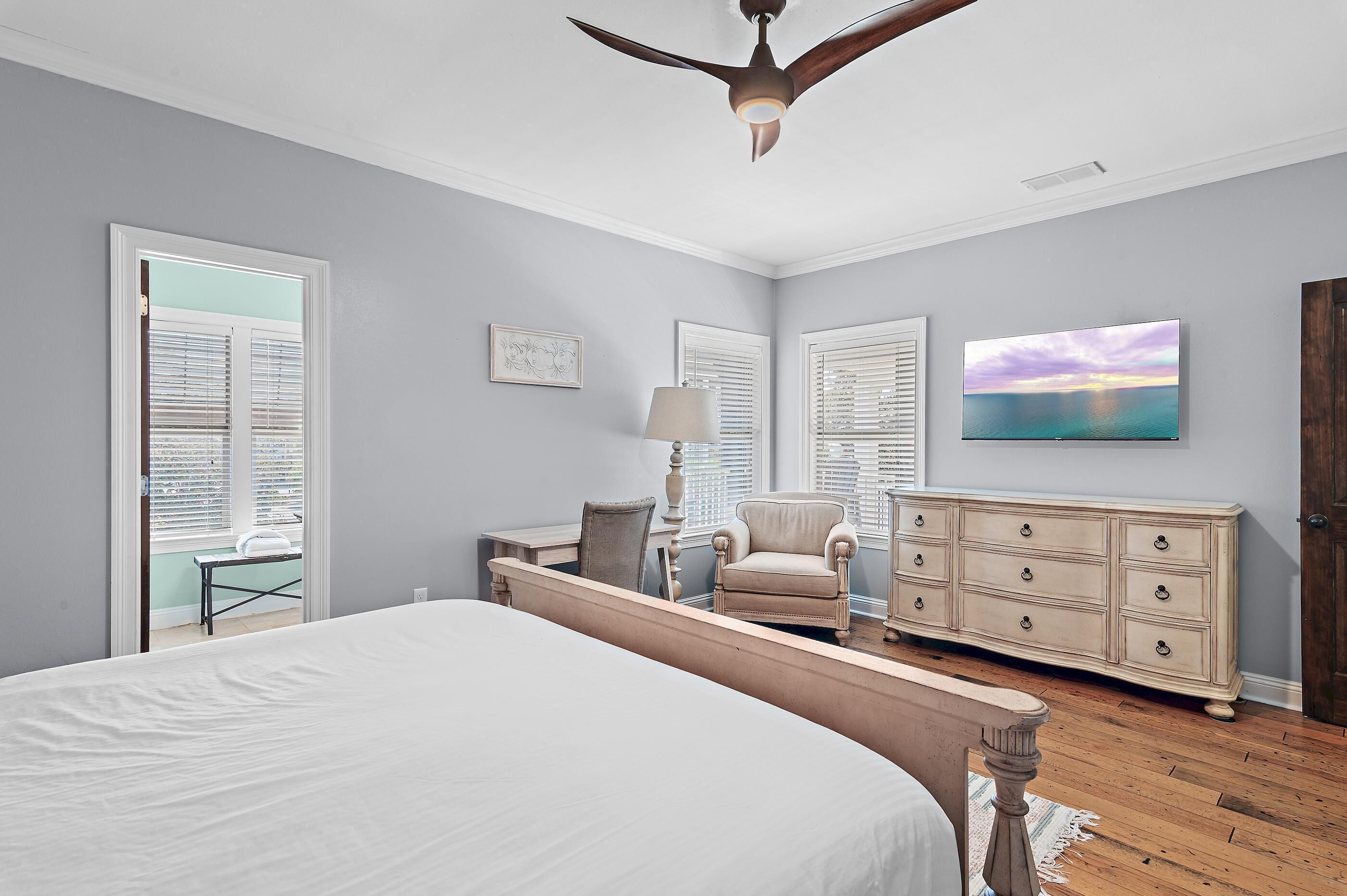 A bedroom with a bed, a desk, a chair, a dresser, and a ceiling fan.