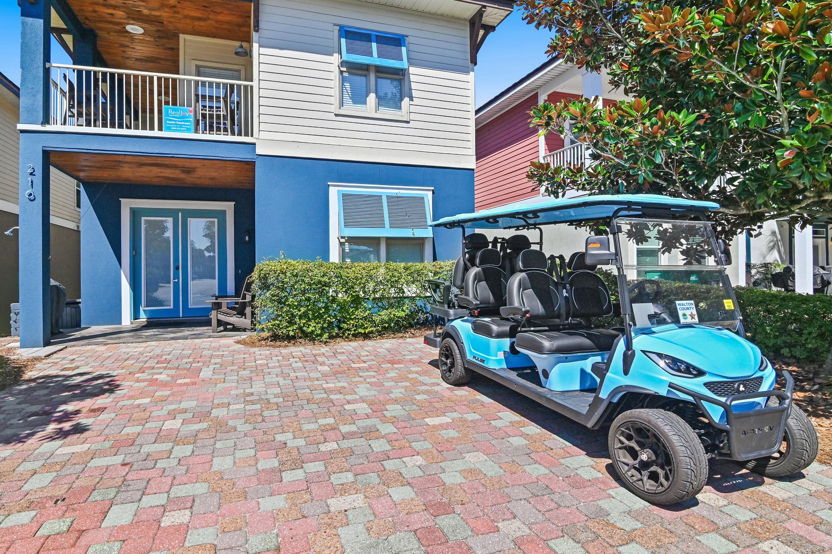 A blue and white building with a gated entrance, a blue golf cart parked in front, and a brick-paved driveway.