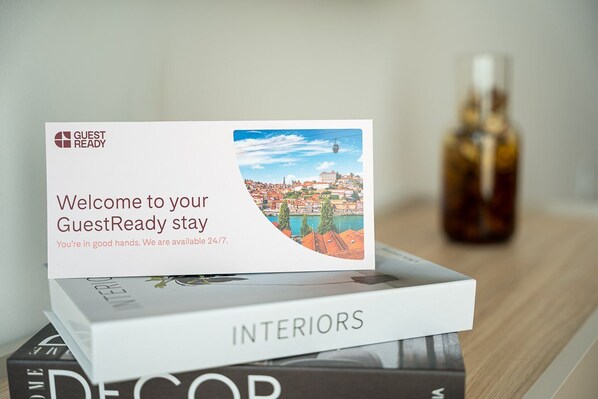 A welcome card for a GuestReady stay with a scenic city view, a bottle, and books on a table.