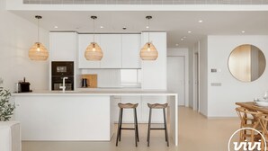 Una cocina moderna con armarios blancos, una isla central con taburetes y tres lámparas colgantes de mimbre.
